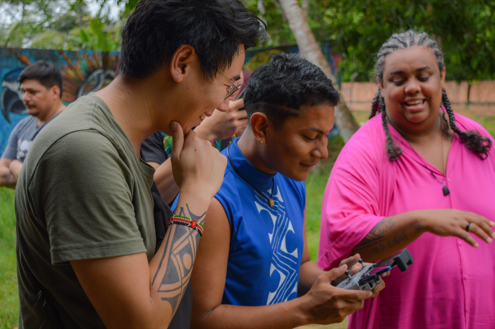 Jovens reunidos observam juntos a tela de uma câmera, num ambiente ao ar livre